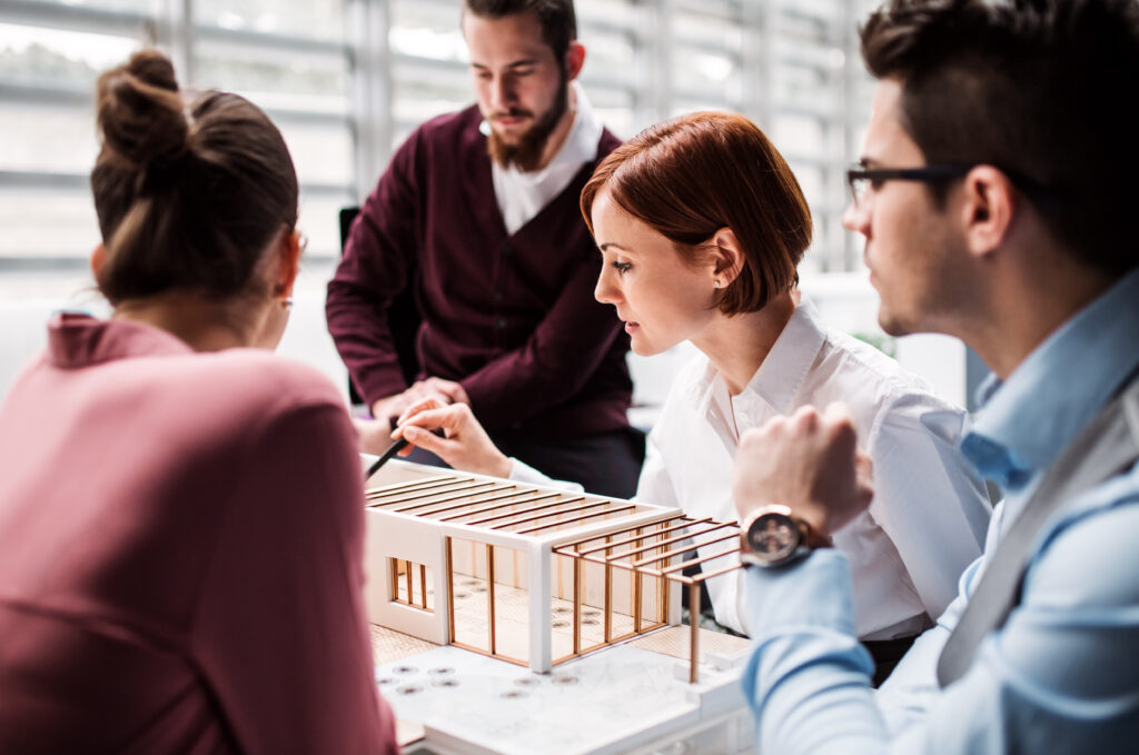 Group of young architects with model of a house standing in office, talking.